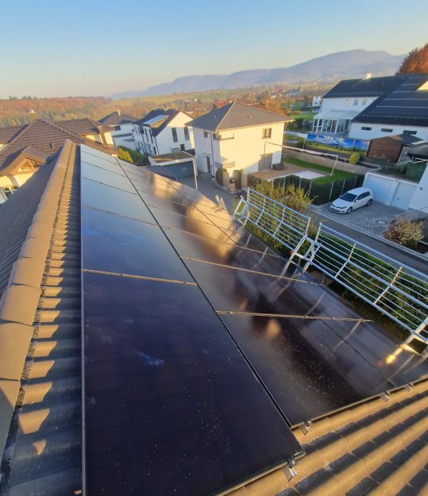 Solarmodule auf einem Satteldach im Abendlicht, dahinter Häuser und Hügel