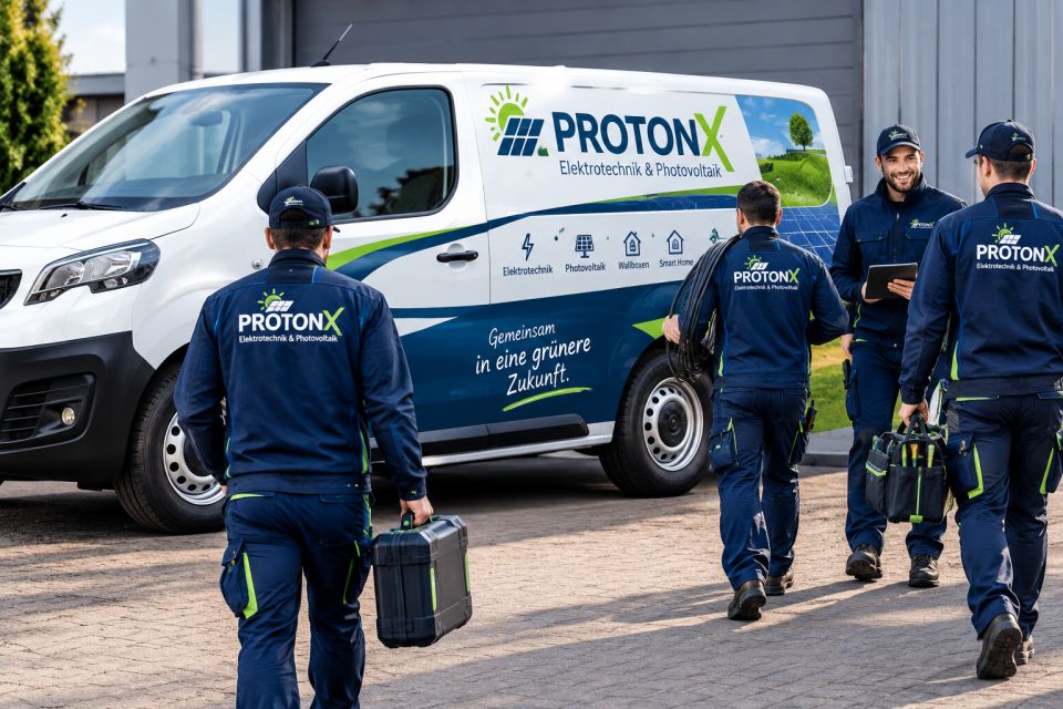 ProtonX-Team in dunkelblauer Arbeitskleidung mit Werkzeugkoffern vor einem Firmenwagen